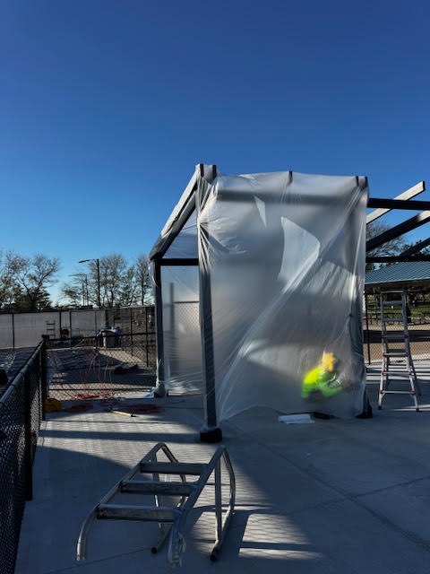 Nearby structure wrapped in plastic sheeting to protect it from overspray